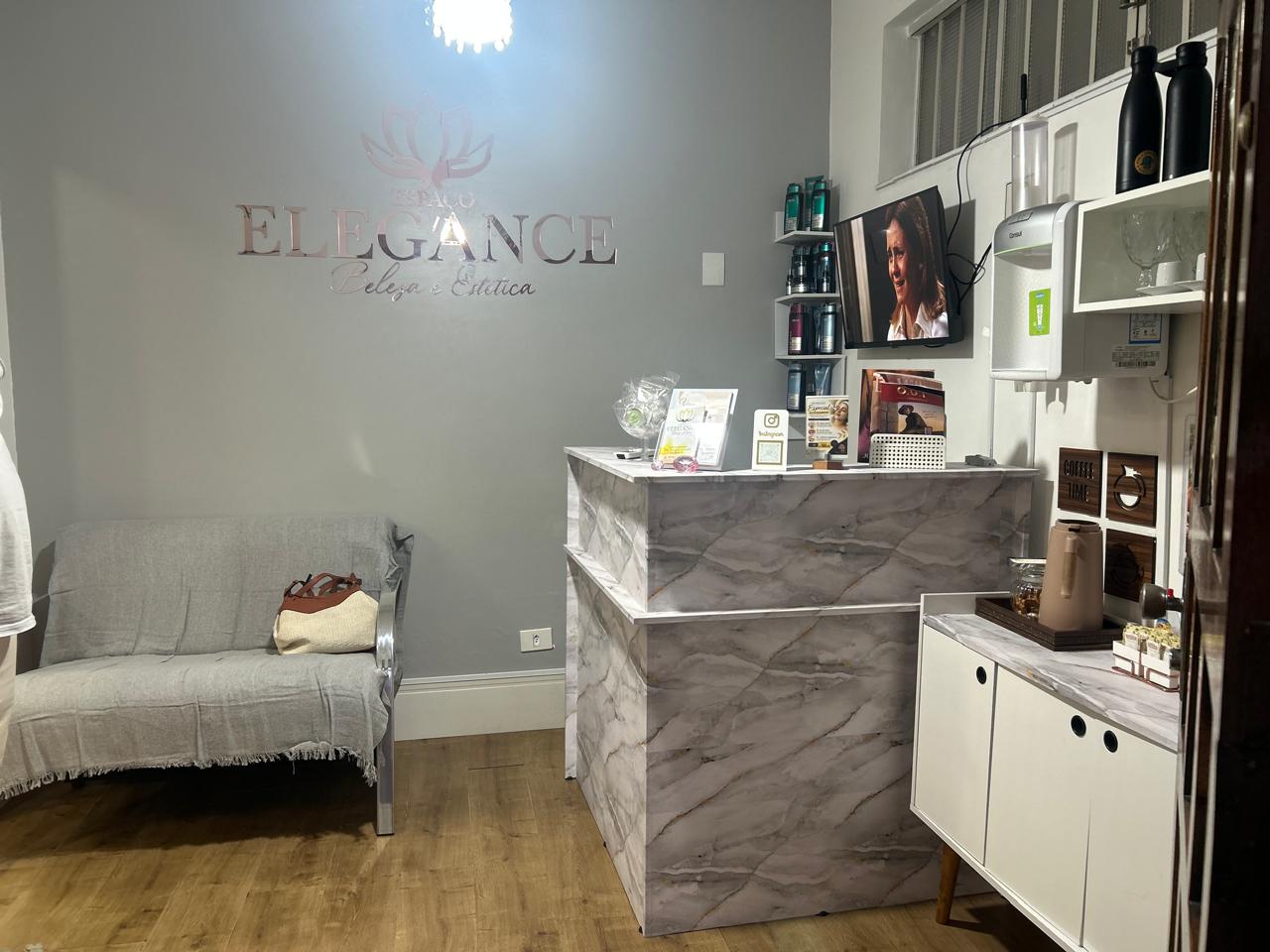 Recepção do Espaço Elegance, com o logo na parede, sofá de espera e balcão de atendimento