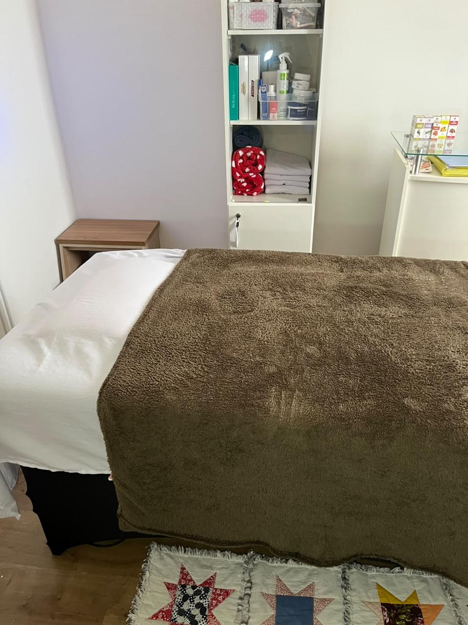 Maca de estética do Espaço Elegance, com manta, toalhas limpas e prateleira de produtos de tratamento